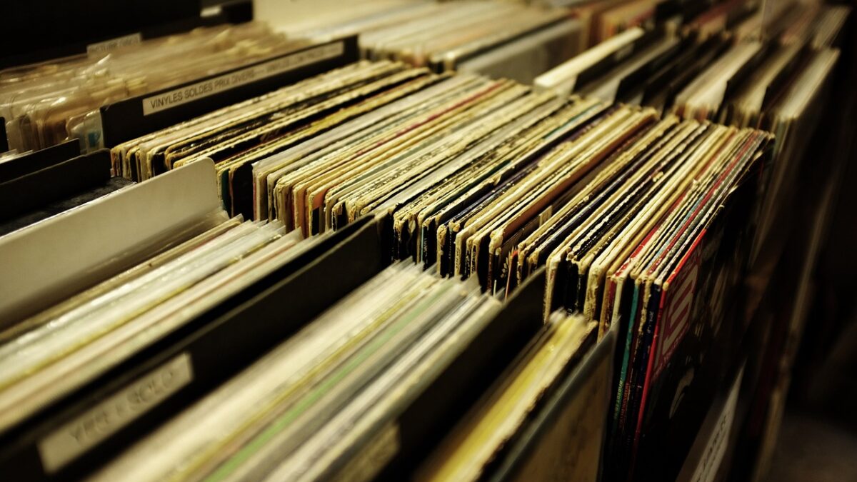 Vinyl-Schallplatten (LP) stehen senkrecht in Sortierfächern eines Secondhand-Plattenladens, im Vordergrund Pappschilder mit Kategorienamen.