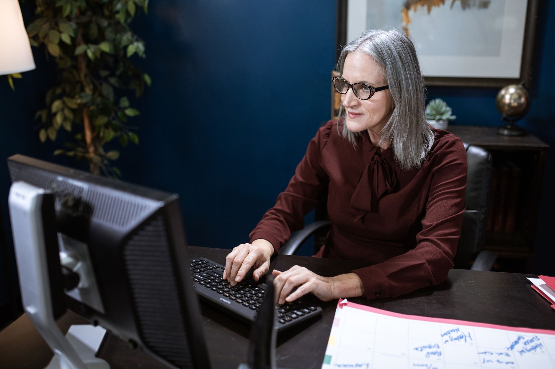 Eine Frau mit Brille arbeitet an einem Desktop-Computer an einem Schreibtisch.