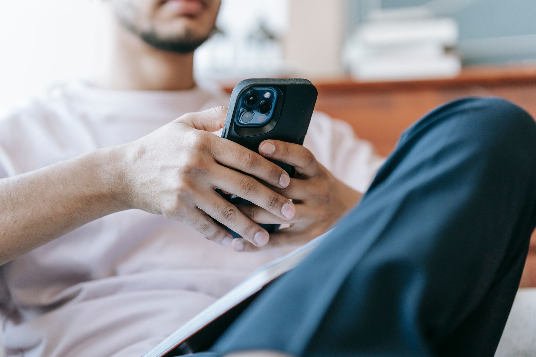 Person auf einem Sofa hält ein Smartphone mit schwarzer Hülle in beiden Händen, im Hintergrund ein unscharfes Wohnzimmer.